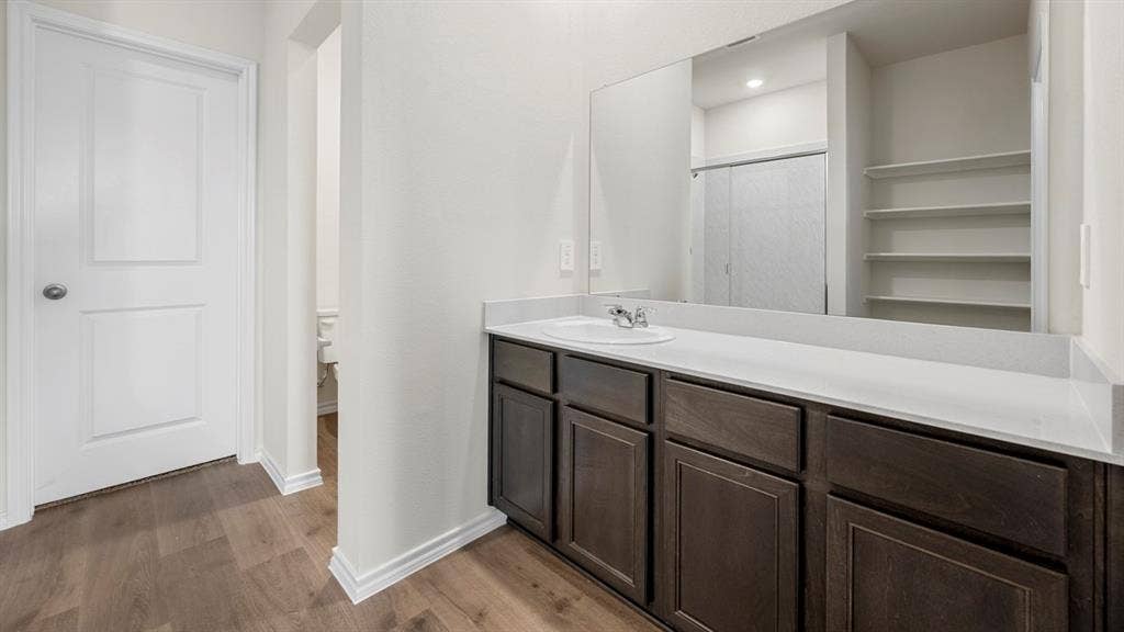 5033 Shumard Drive, Lindale, TX 75771 Wood-finish flooring, white panel door, dark wood-tone vanity, integrated sink, and a large wall-mounted mirror