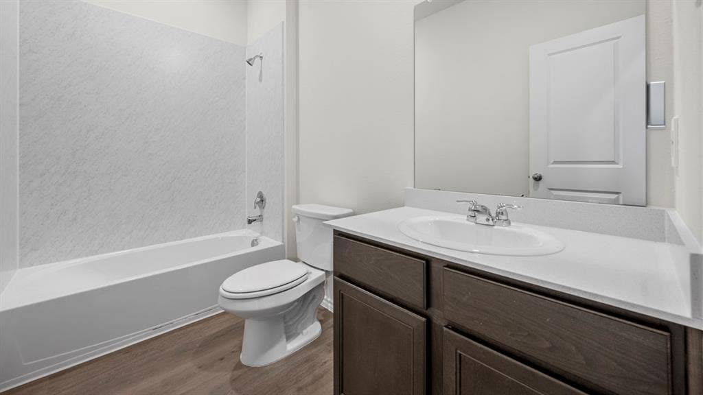 5033 Shumard Drive, Lindale, TX 75771 Bathroom featuring a full vanity with a white countertop and wood-finish cabinetry, a white toilet, and a white bathtub with a shower and surround