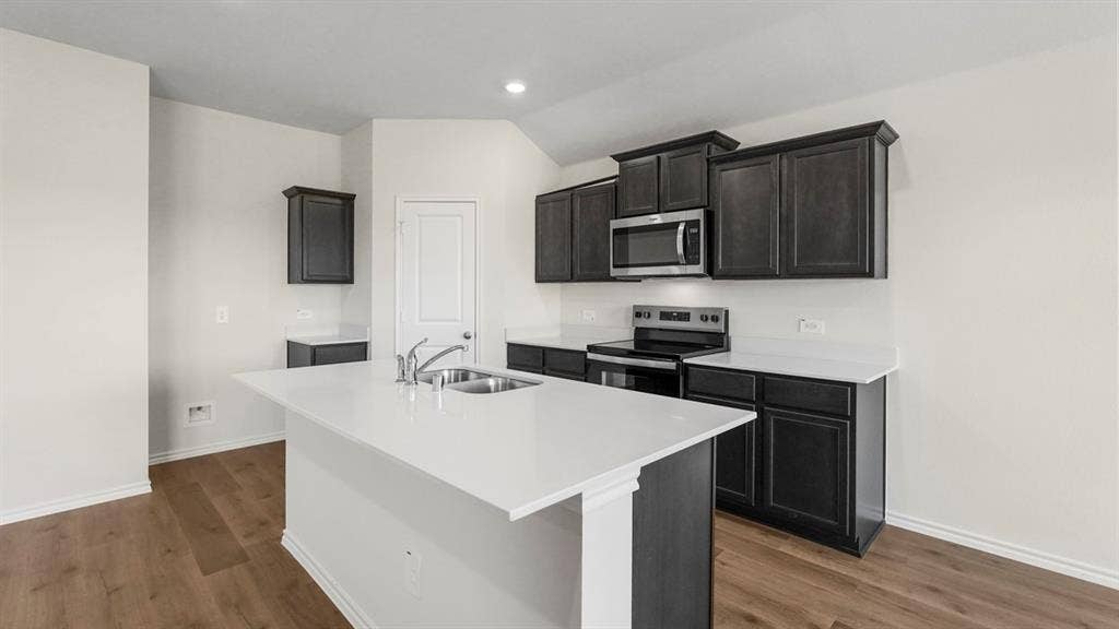 219 Yates Street, Bullard, TX 75757 Kitchen featuring a central island with an undermount double basin sink, stainless steel appliances, dark wood-finish cabinetry, white countertops, and wood-finish flooring