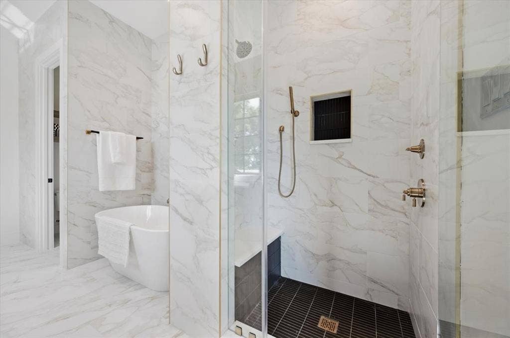 4320 Concho Street, Dallas, TX 75206 Freestanding soaking tub, walk-in shower with glass enclosure, integrated shower niche, and brushed brass fixtures