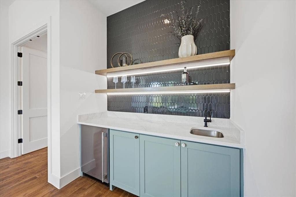 4320 Concho Street, Dallas, TX 75206 Built-in wet bar featuring a beverage refrigerator, light blue cabinetry, under-cabinet lighting, and a dark hexagonal tile backsplash
