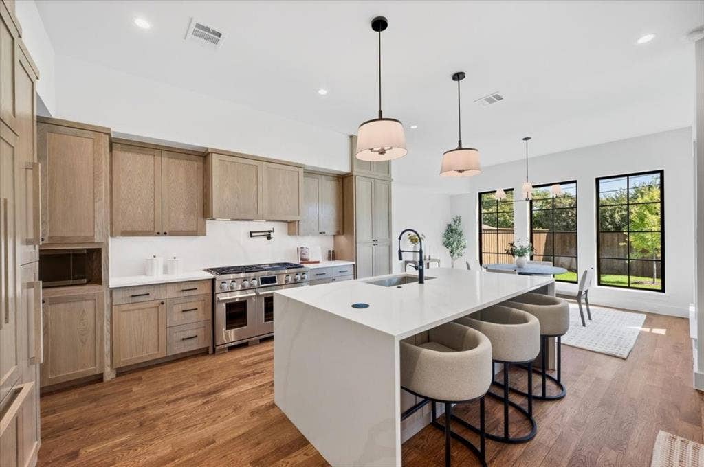 4320 Concho Street, Dallas, TX 75206 Hardwood flooring throughout, a large kitchen island with counter seating, stainless steel appliances, light wood-finish cabinetry, and black-framed windows