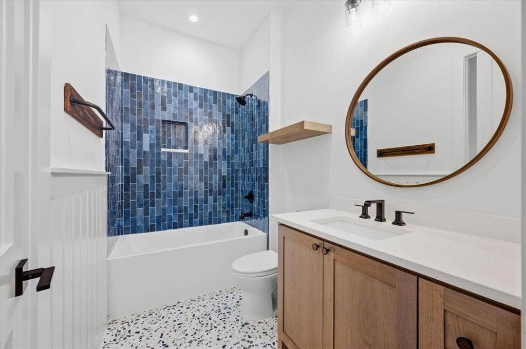 4320 Concho Street, Dallas, TX 75206 Bathroom featuring blue subway tile shower surround, integrated shower niche, wood-finish vanity with countertop, oval mirror, and speckled flooring