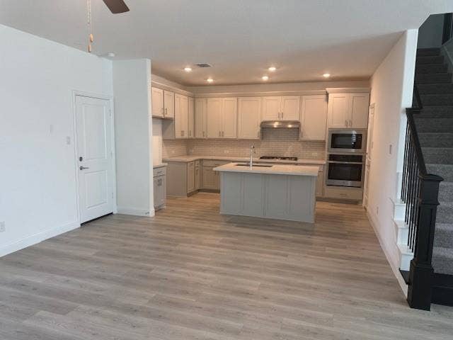109 North Sky Drive, Celina, TX 75009 Open-concept layout featuring light wood-finish flooring, a contemporary kitchen island with seating, stainless steel appliances, a tiled backsplash, and recessed lighting