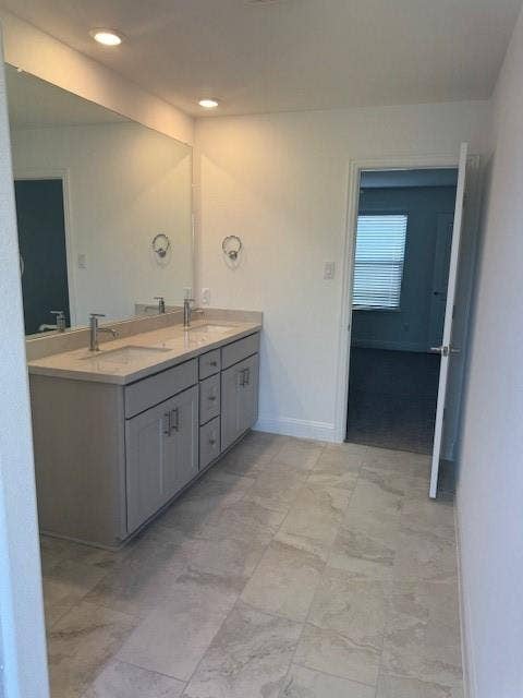 109 North Sky Drive, Celina, TX 75009 Spacious bathroom featuring a double vanity with grey cabinetry, stone-finish countertop, dual undermount sinks, and an expansive wall-mounted mirror