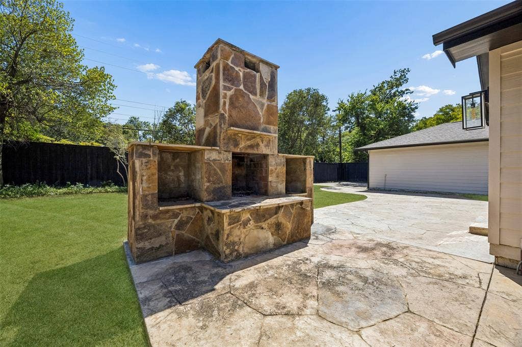 5610 Forest Lane, Dallas, TX 75230 Expansive backyard featuring a stone outdoor fireplace, stamped concrete patio, manicured lawn, and privacy fencing