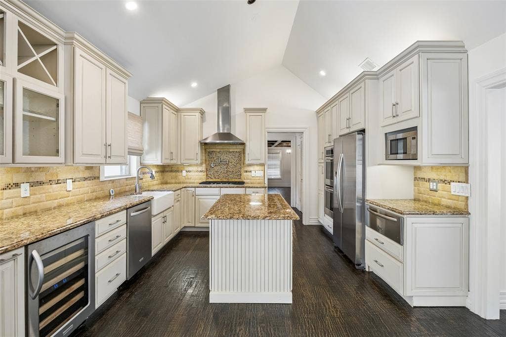 5610 Forest Lane, Dallas, TX 75230 Kitchen featuring a vaulted ceiling, dark wood-finish flooring, white cabinetry, integrated stainless steel appliances, and a central island with a wood-finish countertop