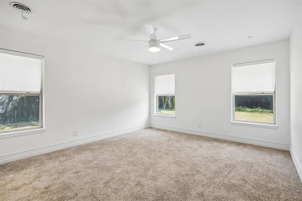 5610 Forest Lane, Dallas, TX 75230 Neutral-toned carpet flooring, crisp white walls, three windows with roller shades, and a ceiling fan with integrated lighting