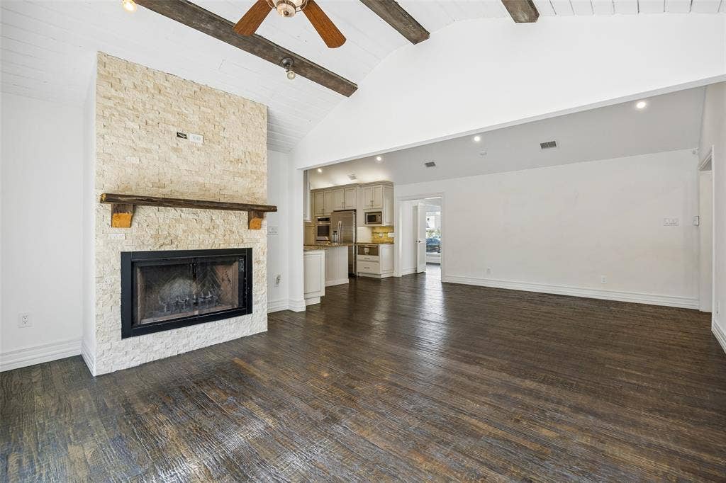 5610 Forest Lane, Dallas, TX 75230 Vaulted ceiling with exposed wood beams, wood-finish flooring, stone-clad fireplace with wood mantel, recessed lighting, and a ceiling fan