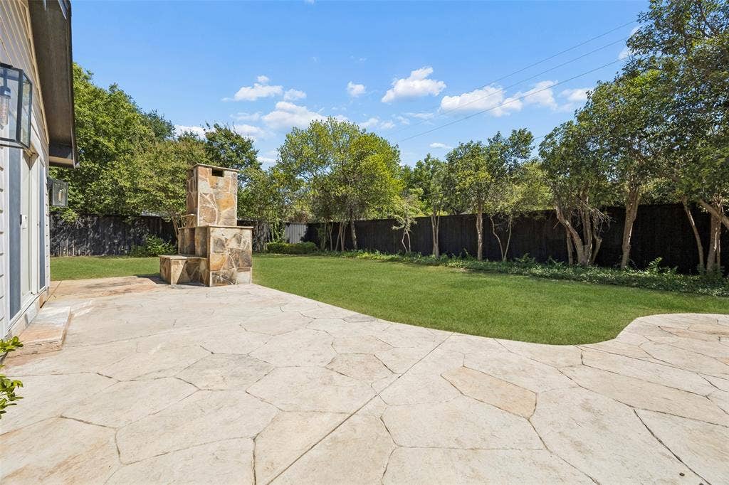 5610 Forest Lane, Dallas, TX 75230 Flagstone patio with a built-in stone fireplace, expansive lawn, and perimeter fencing