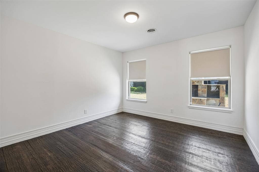 5610 Forest Lane, Dallas, TX 75230 Dark wood-finish flooring, white walls, two windows with roller shades, and a ceiling-mounted light fixture