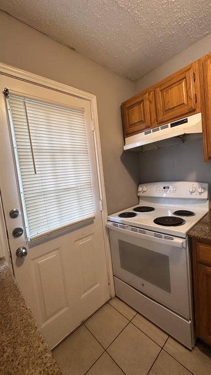 White electric range, wood cabinetry, and tile flooring