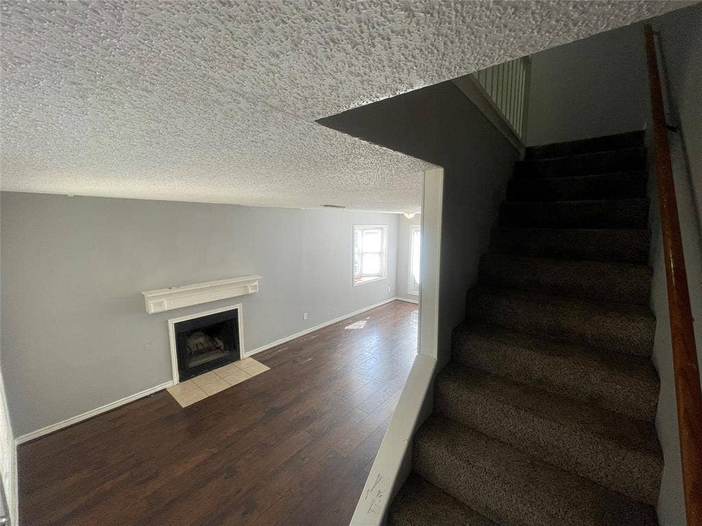 Wood-finish flooring, fireplace with a decorative mantel, neutral-toned walls, and a staircase with a wooden handrail