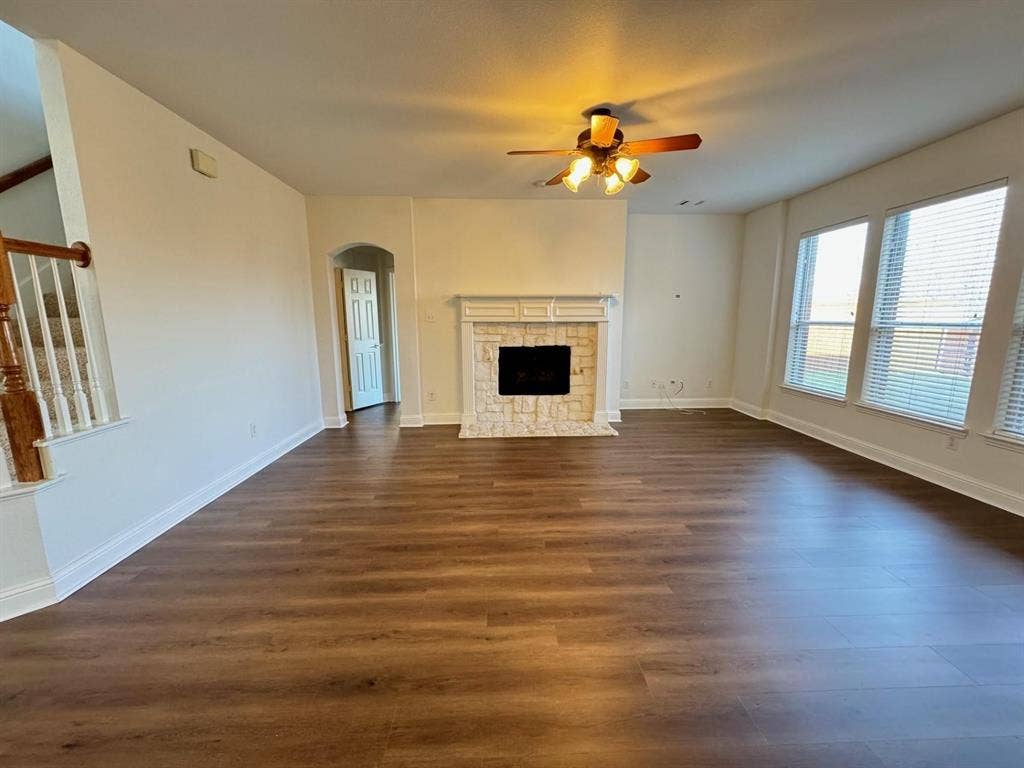 4531 Oak Shores Drive, Plano, TX 75024 Spacious living area featuring wood-finish flooring, a fireplace with a stone surround, multiple windows, and a ceiling fan