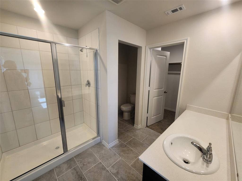 1302 Breezy Oak Drive, Nevada, TX 75173 Tiled shower enclosure with sliding glass doors, single vanity with integrated sink and chrome faucet, and tiled flooring