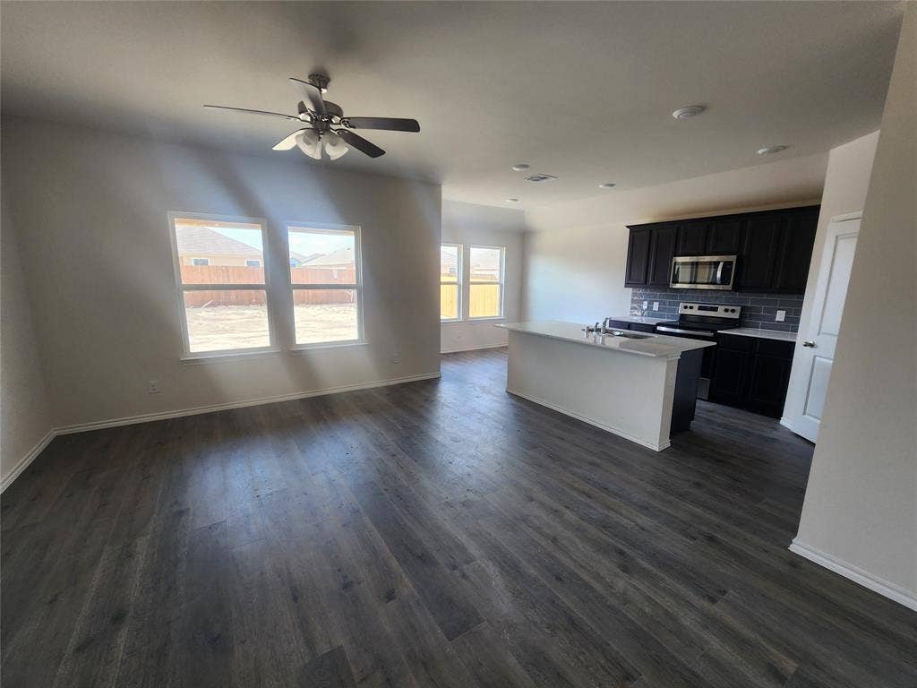 1302 Breezy Oak Drive, Nevada, TX 75173 Spacious open-concept layout featuring wood-finish flooring, a kitchen island with a built-in sink, dark cabinetry, and a subway tile backsplash