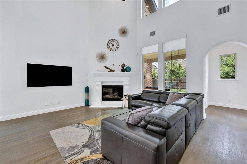 625 Quarter Horse Lane, Frisco, TX 75036 Soaring ceiling with high windows, fireplace with white mantel, wood-finish flooring, and arched doorway
