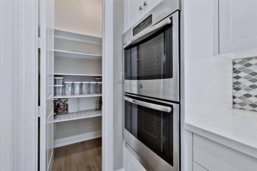 625 Quarter Horse Lane, Frisco, TX 75036 Stainless steel double wall ovens, white cabinetry, white countertop, geometric tile backsplash, and a walk-in pantry with wood-finish flooring