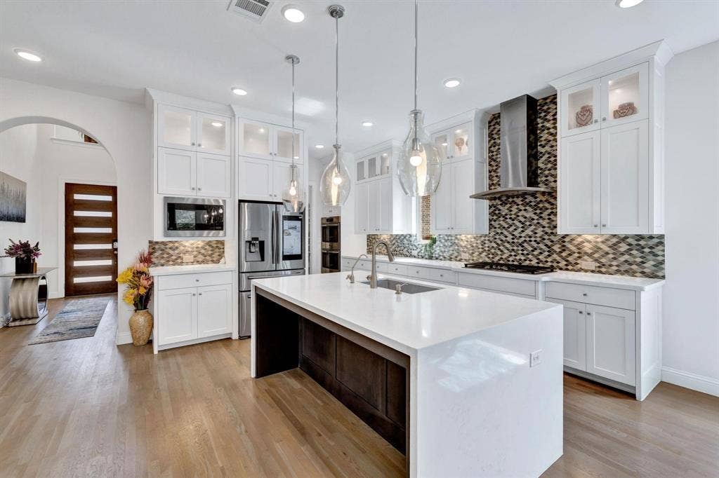 625 Quarter Horse Lane, Frisco, TX 75036 Wood-finish flooring throughout, white cabinetry, stainless steel appliances, mosaic tile backsplash, and a large central island