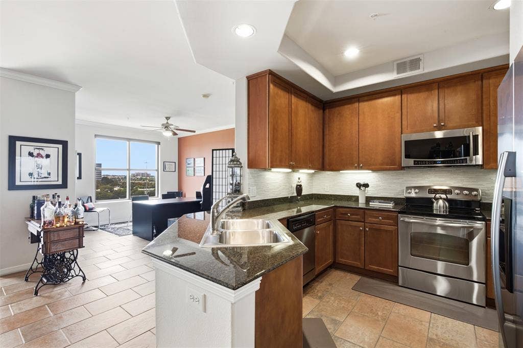 330 Las Colinas Boulevard E, #1216, Irving, TX 75039 Kitchen featuring wood cabinetry, stainless steel appliances, granite countertops, and a tile backsplash