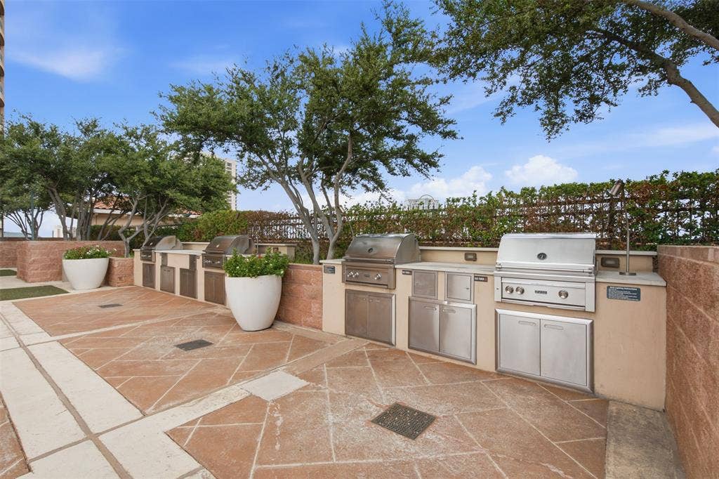 330 Las Colinas Boulevard E, #1216, Irving, TX 75039 Expansive outdoor patio with stone paver flooring, multiple built-in stainless steel grills, integrated cabinetry, and lush perimeter landscaping