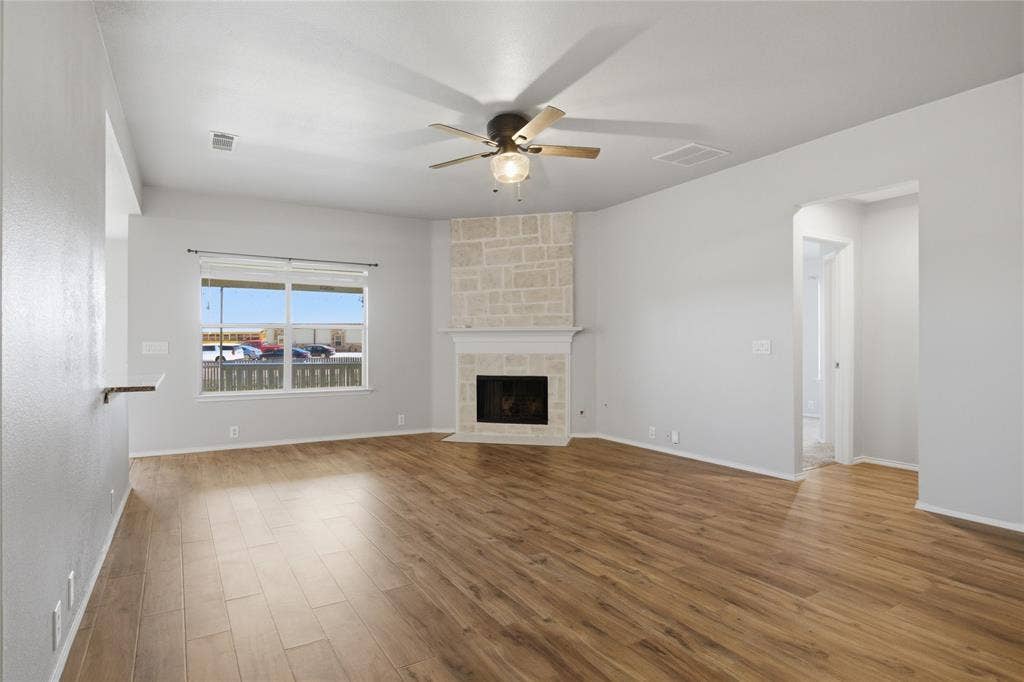 217 Ame Lane, Royse City, TX 75189 Expansive living area featuring wood-finish flooring, a stone-clad fireplace with a mantel, a ceiling fan, and a large window