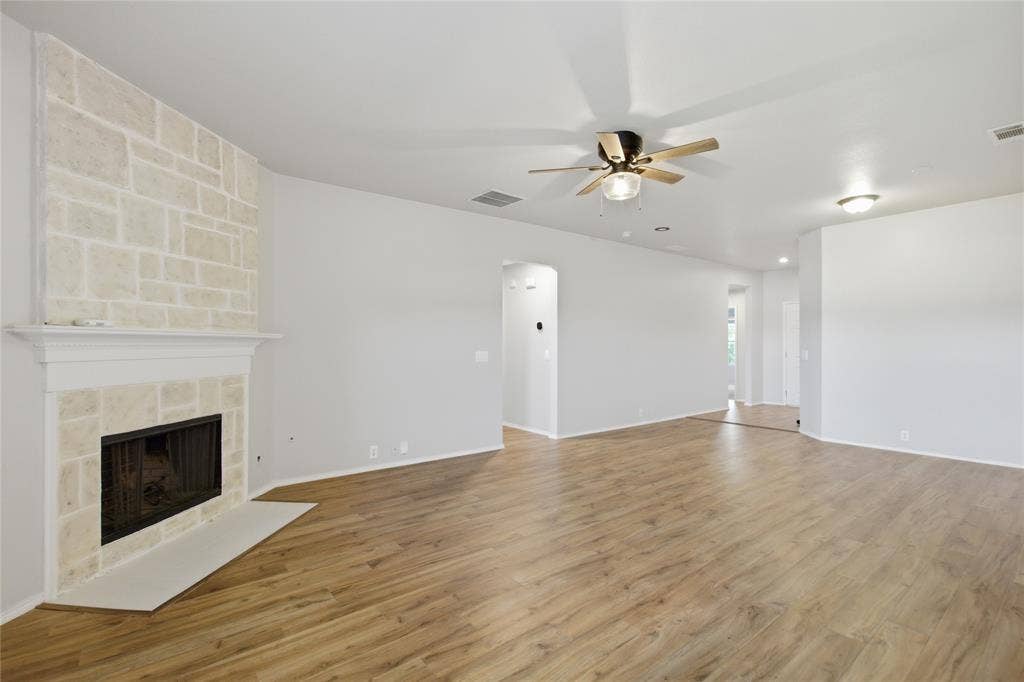217 Ame Lane, Royse City, TX 75189 Spacious room featuring a stone-clad fireplace with a classic mantel, wood-finish flooring, and a ceiling fan with integrated lighting
