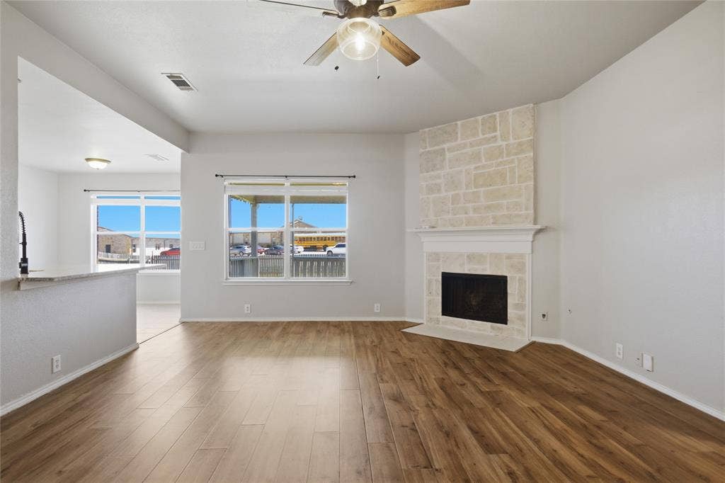 217 Ame Lane, Royse City, TX 75189 Wood-finish flooring, stone-clad fireplace, ceiling fan with light fixture, large windows, and a breakfast bar with a sink