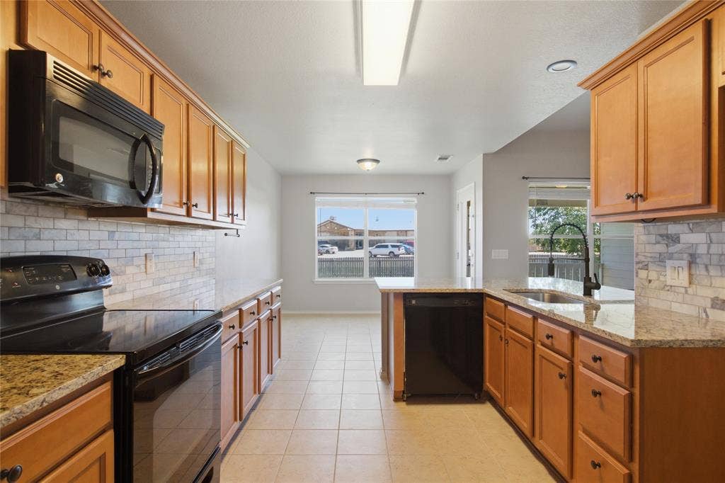 217 Ame Lane, Royse City, TX 75189 Well-appointed kitchen featuring wood-finish cabinetry, black appliances, granite countertops, tile backsplash, and tile flooring