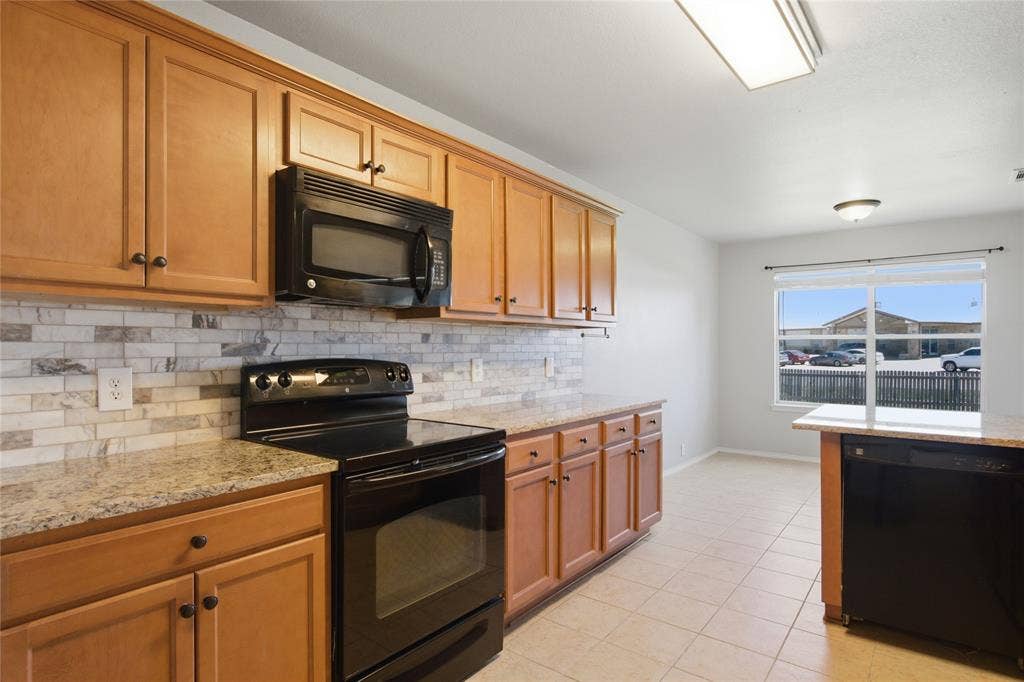217 Ame Lane, Royse City, TX 75189 Wood-finish cabinetry, tile backsplash, stone-finish countertops, black appliances, and tile flooring