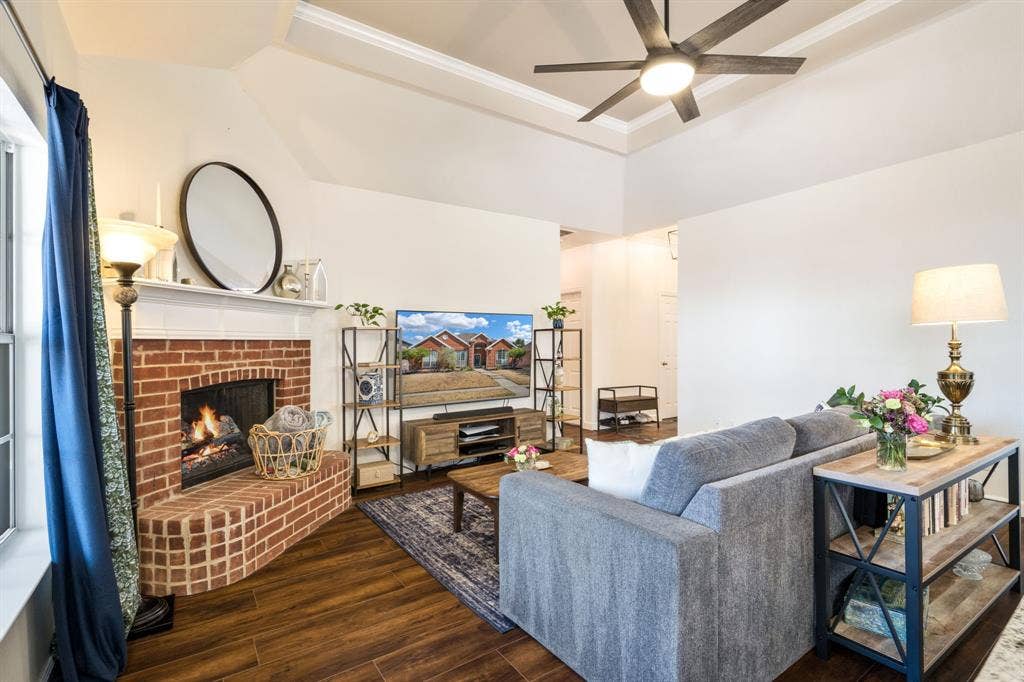 11414 Promenade Road, Frisco, TX 75035 Living area featuring wood-finish flooring, a brick fireplace with a hearth, and a tray ceiling with a ceiling fan