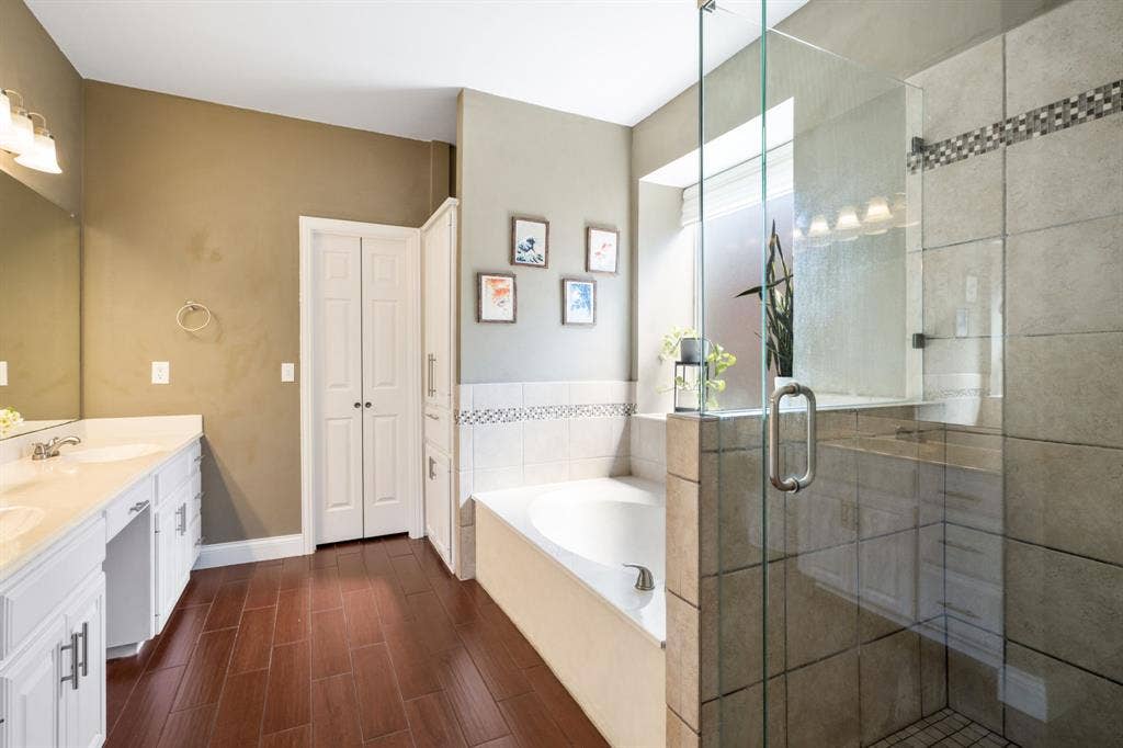 11414 Promenade Road, Frisco, TX 75035 Double vanity with white cabinetry, wood-finish flooring, built-in soaking tub, glass-enclosed shower, and a built-in linen cabinet