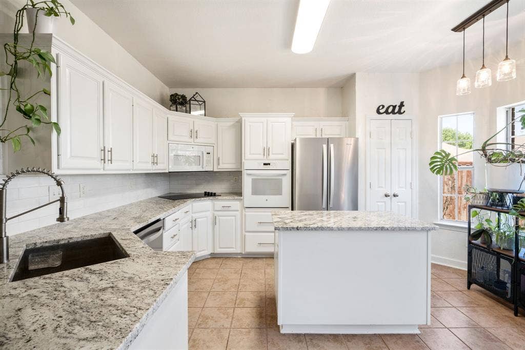 11414 Promenade Road, Frisco, TX 75035 White cabinetry with brushed nickel hardware, light-toned granite countertops, a central island, stainless steel appliances, and tile flooring
