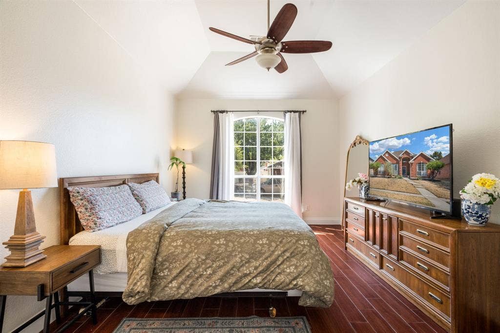11414 Promenade Road, Frisco, TX 75035 Vaulted ceiling with a ceiling fan, arched window with drapes, wood-finish flooring, and a built-in wood-finish dresser