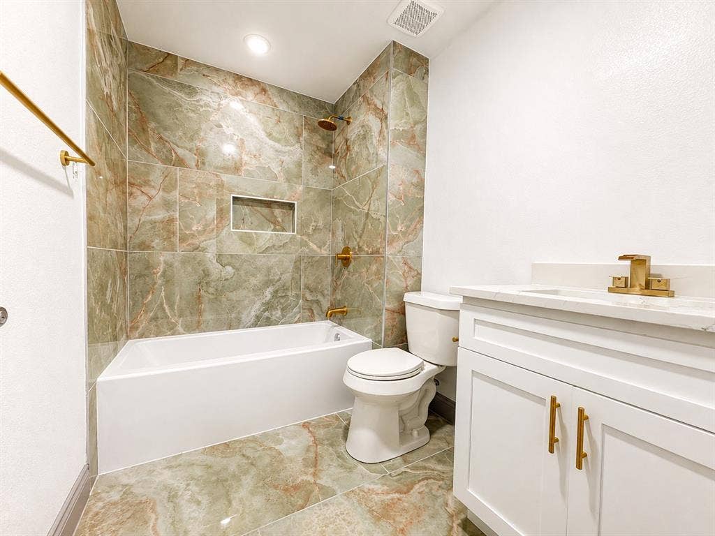 4316 Woodbluff Drive, Mesquite, TX 75150 Modern bathroom featuring floor-to-ceiling green and brown marbled tile, white built-in bathtub, and a built-in shower niche