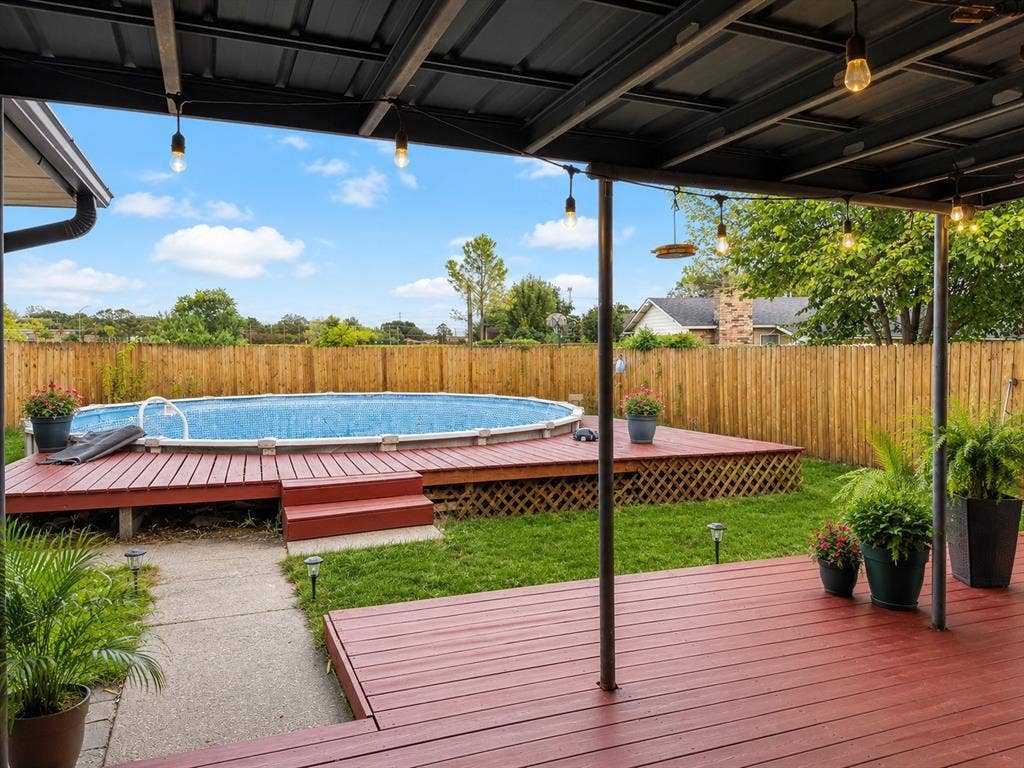 4316 Woodbluff Drive, Mesquite, TX 75150 Vertually stagedCovered patio with string lighting, red-stained wood decking, and an above-ground pool with surrounding wood deck