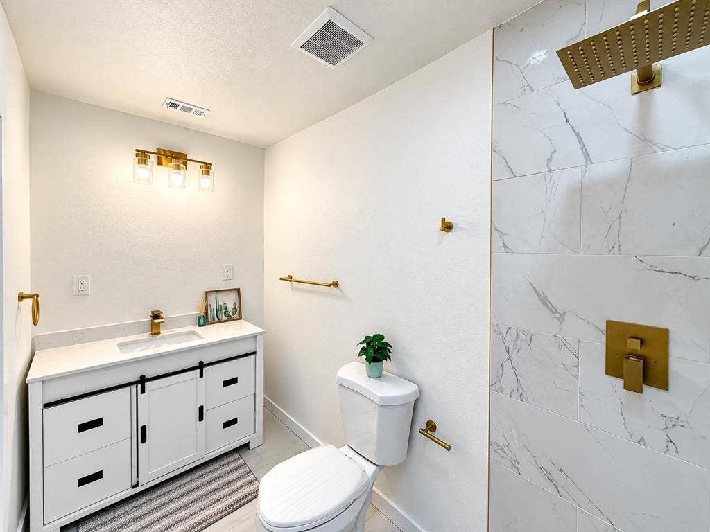 1737 Alta Vista Street, Mesquite, TX 75149 Bathroom featuring a white vanity with sliding cabinet doors, stone-finish countertop, brass-tone hardware and fixtures, and a shower surround with large-format patterned wall tile