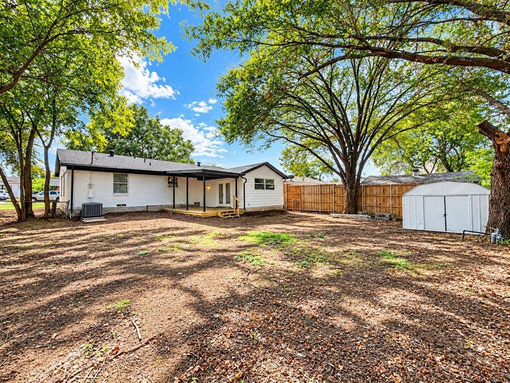 1737 Alta Vista Street, Mesquite, TX 75149 Expansive backyard featuring mature shade trees, a wooden privacy fence, a covered rear patio, and an external storage structure