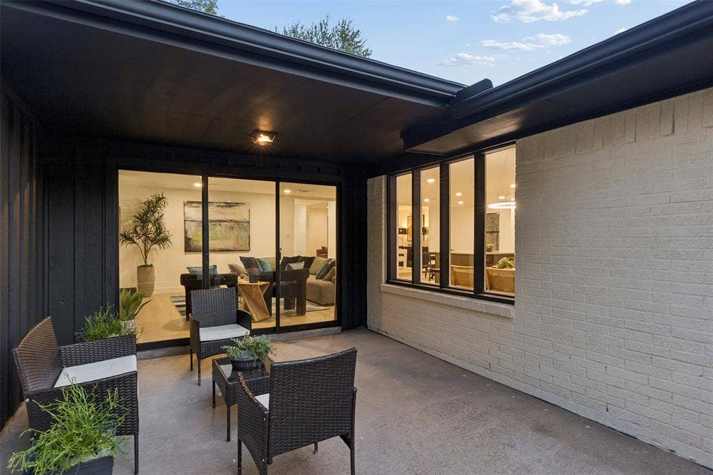 2133 Oak Valley Lane, Dallas, TX 75232 Concrete patio with a dark overhang, white painted brick exterior, and large sliding glass doors