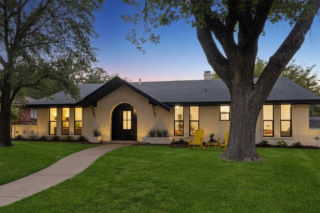 2133 Oak Valley Lane, Dallas, TX 75232 exterior with an arched entryway, dark trim windows, a paved walkway, and mature trees
