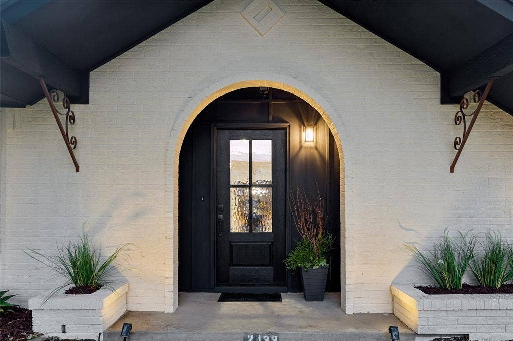 2133 Oak Valley Lane, Dallas, TX 75232 Arched entryway featuring a dark-paneled door with glass inserts, brick exterior, and decorative wrought iron brackets