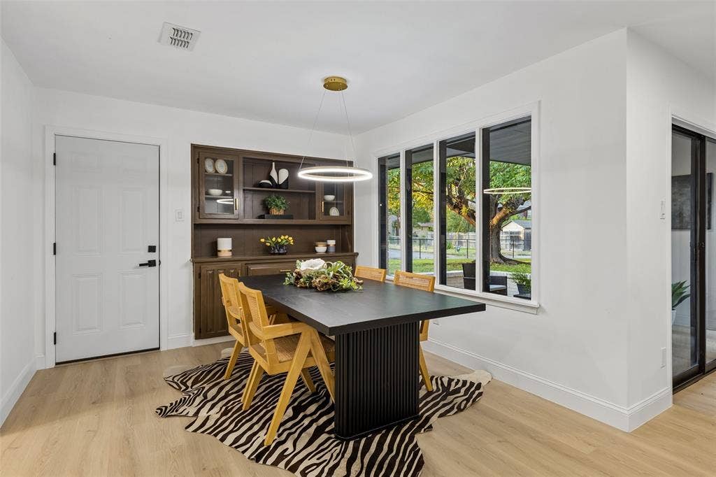 2133 Oak Valley Lane, Dallas, TX 75232 Light wood-finish flooring, built-in dark wood cabinetry with glass fronts, a contemporary linear chandelier, and multiple rectangular windows