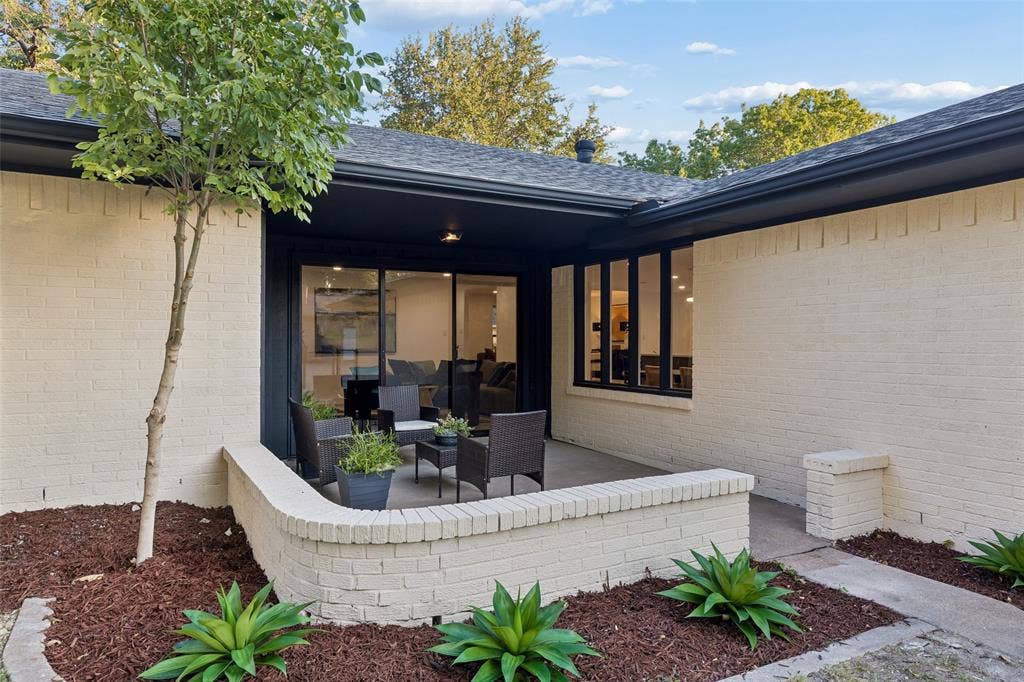 2133 Oak Valley Lane, Dallas, TX 75232 Brick exterior with dark trim accents, covered patio, large sliding glass doors, and a manicured landscape