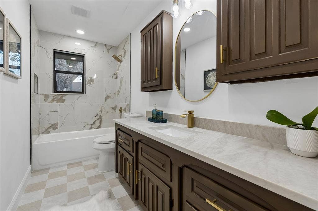2133 Oak Valley Lane, Dallas, TX 75232 Spacious bathroom featuring a built-in bathtub with a tile surround, dark wood-finish cabinetry, a single vanity with an undermount sink, and a circular mirror