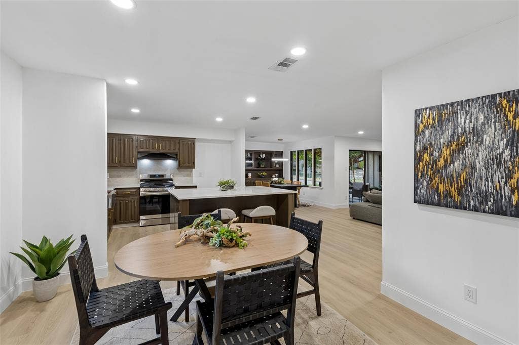 2133 Oak Valley Lane, Dallas, TX 75232 Open-concept interior featuring recessed lighting, light wood-finish flooring, a kitchen with dark wood cabinetry, a center island with counter seating, and stainless steel appliances