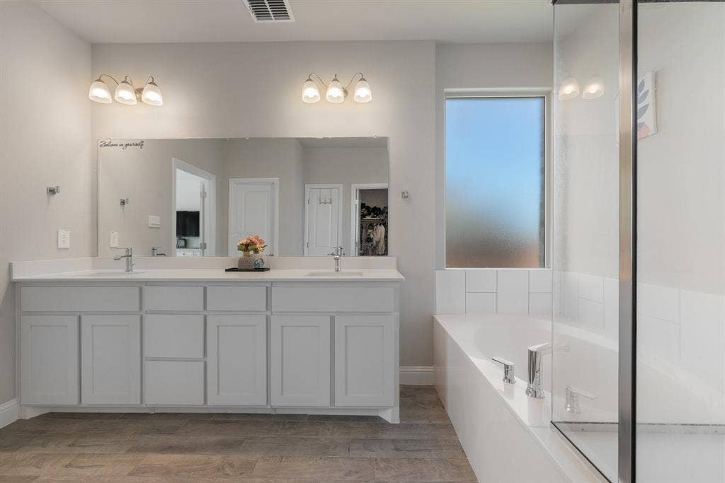 Bathroom with double vanity, a tub, and light wood finished floors