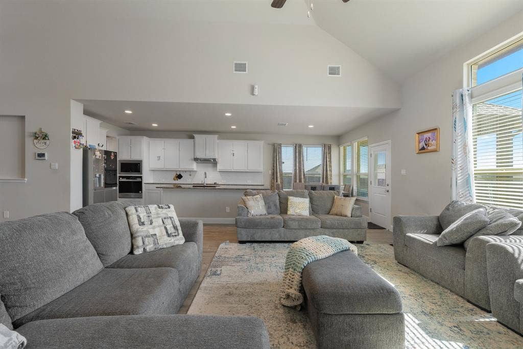 Living area featuring high vaulted ceiling, healthy amount of natural light, a ceiling fan, wood finished floors, and recessed lighting