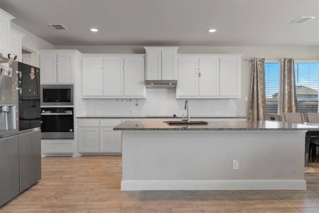 Kitchen featuring appliances with stainless steel finishes, dark stone countertops, white cabinetry, light wood-style flooring, and recessed lighting