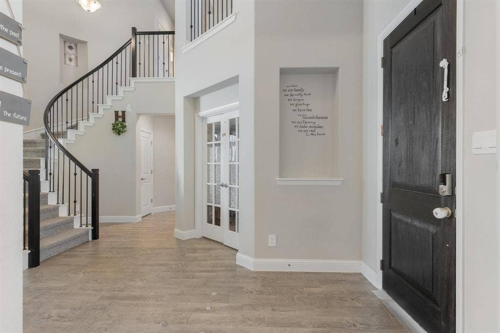 Entryway with stairway, light wood-style floors, french doors, and a towering ceiling