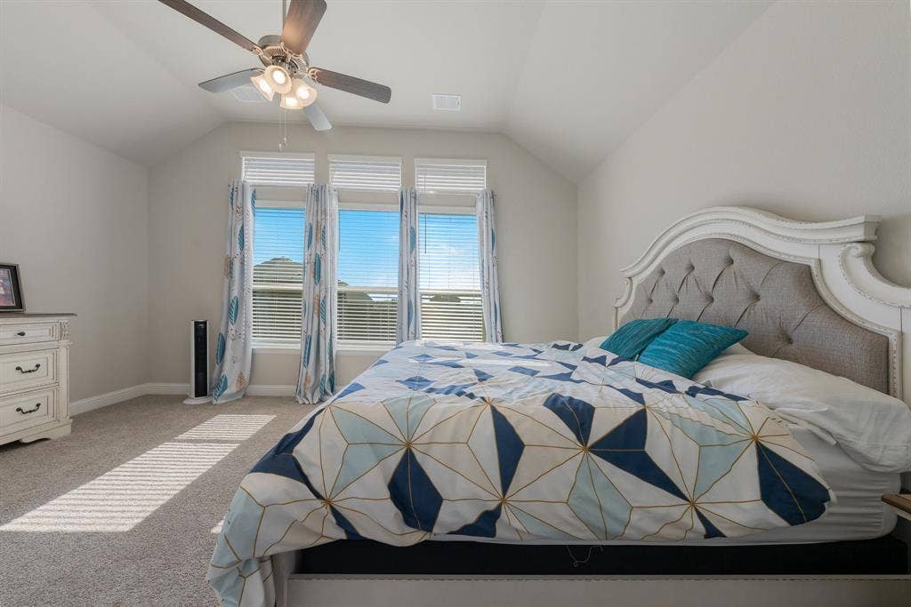 Spacious primary bedroom with lofted ceiling, carpet floors, and ceiling fan